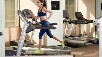 A woman running on a treadmill in a gym with multiple treadmills and a mirrored wall.