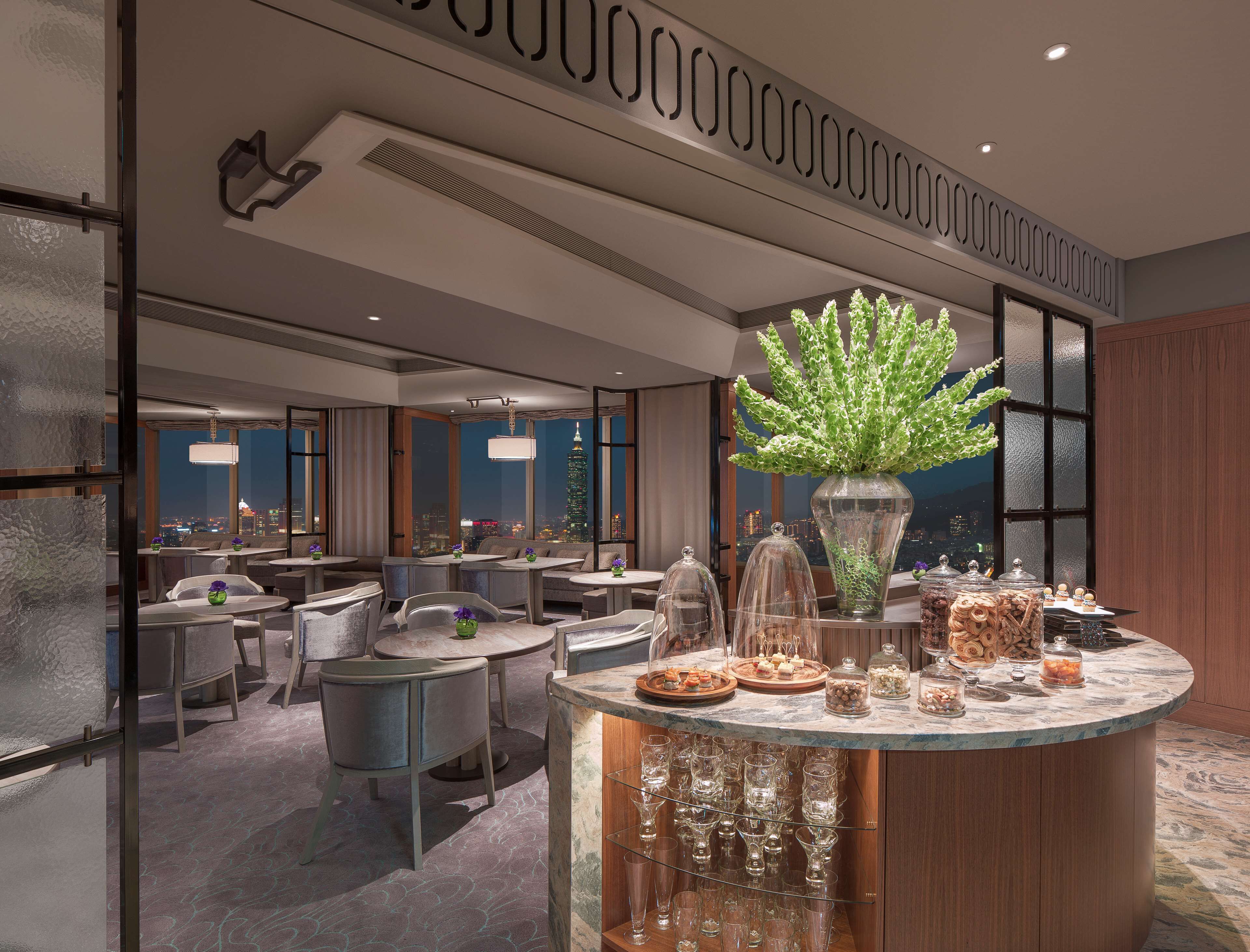 Een moderne hotellobby met een centrale bar, zitgedeeltes en uitzicht op de stad.
