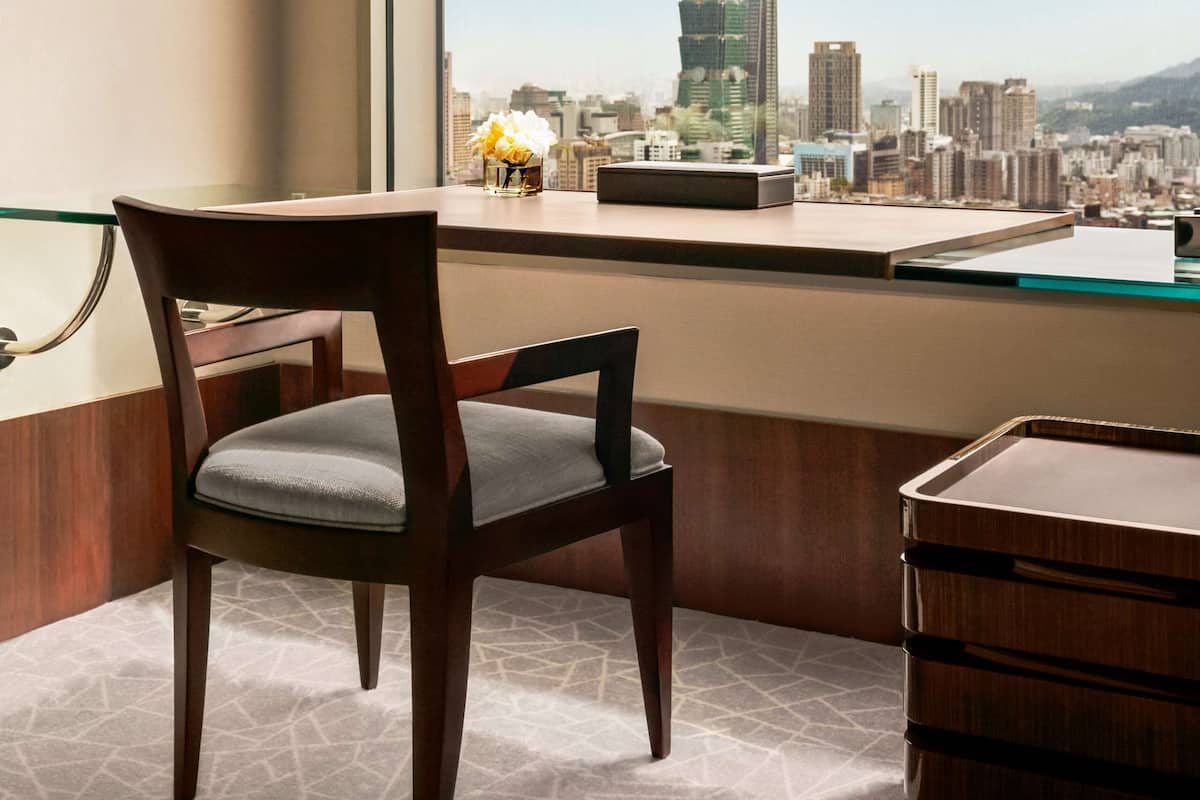 A modern room with a large window, a wooden chair, a small table, and a decorative vase.