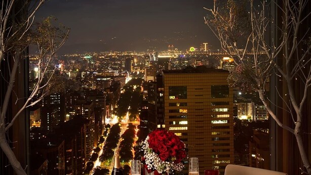 Une table dressée pour deux personnes, avec vue sur la ville, un bouquet de roses rouges et une bouteille de champagne.