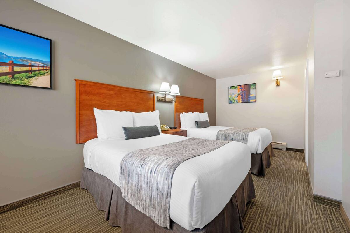 Ein Hotelzimmer mit zwei Betten, einem Holz-Kopfteil, Nachttischlampen, einem Telefon und einem Bild an der Wand.