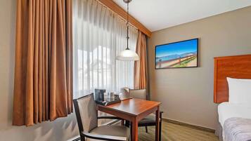 Habitación de hotel con cama, una mesa de comedor con sillas, cafetera y un cuadro en la pared.