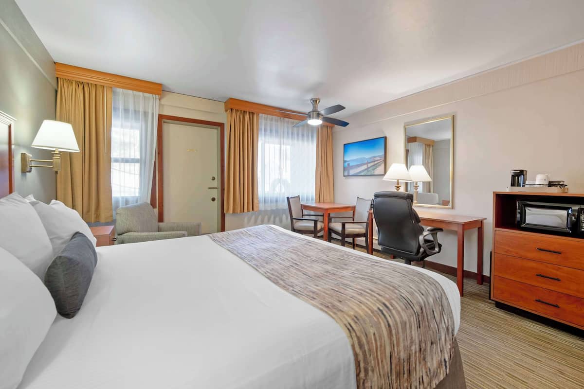 Ein Hotelzimmer mit einem Bett, einem Schreibtisch, einem Sessel, einer Mikrowelle und einem Deckenventilator.