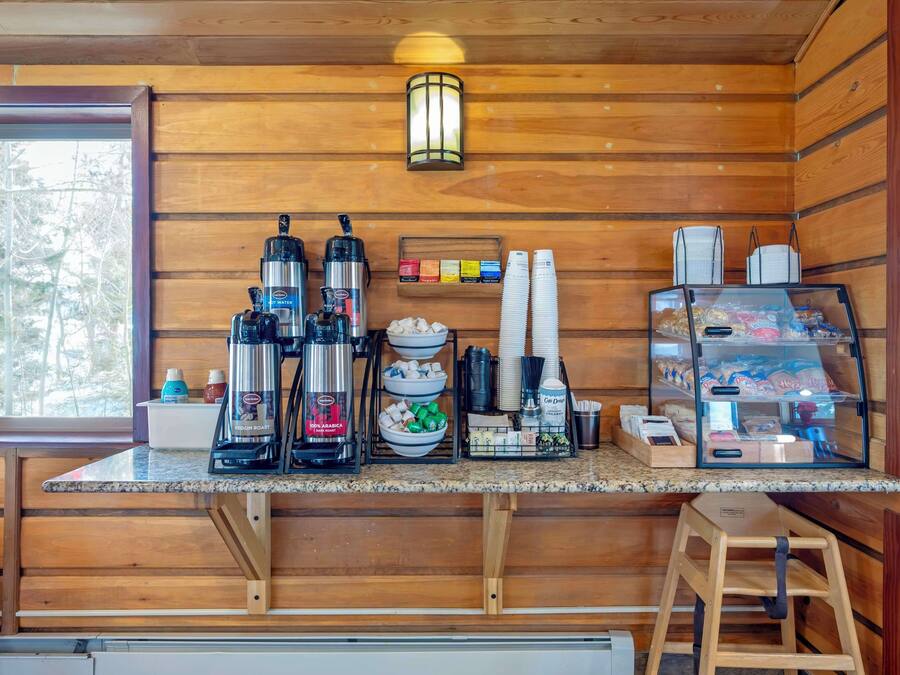 A wooden cabin interior with a kitchen area featuring coffee makers, a coffee station, and a glass display case with snacks.