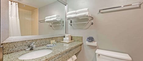 A bathroom with a granite countertop sink, a mirror, a towel rack, a toilet, and a towel dispenser.
