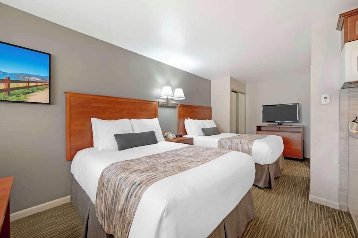 Ein Hotelzimmer mit zwei Betten, einem Fernseher, einem Schreibtisch und einem Bild an der Wand.