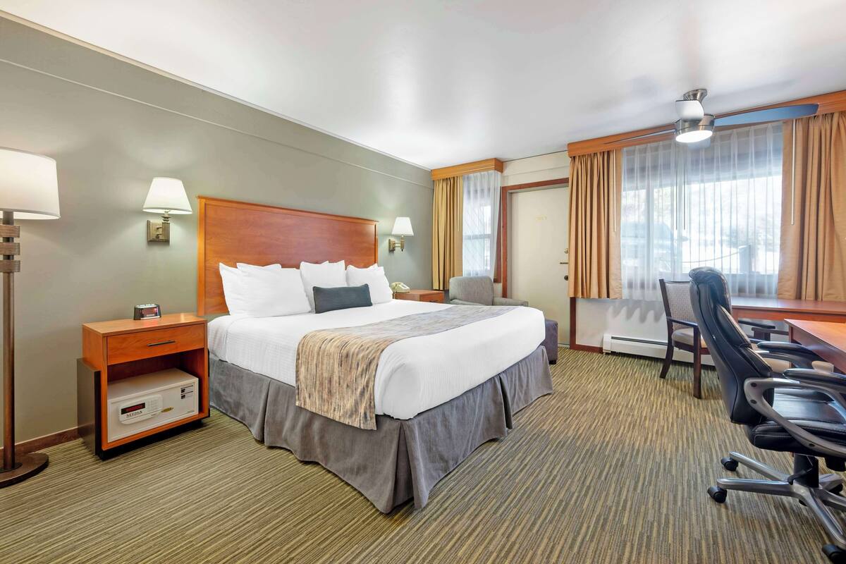 Ein Hotelzimmer mit einem großen Bett, einem Schreibtisch, einem Sessel, einem Nachttisch und einer Lampe.