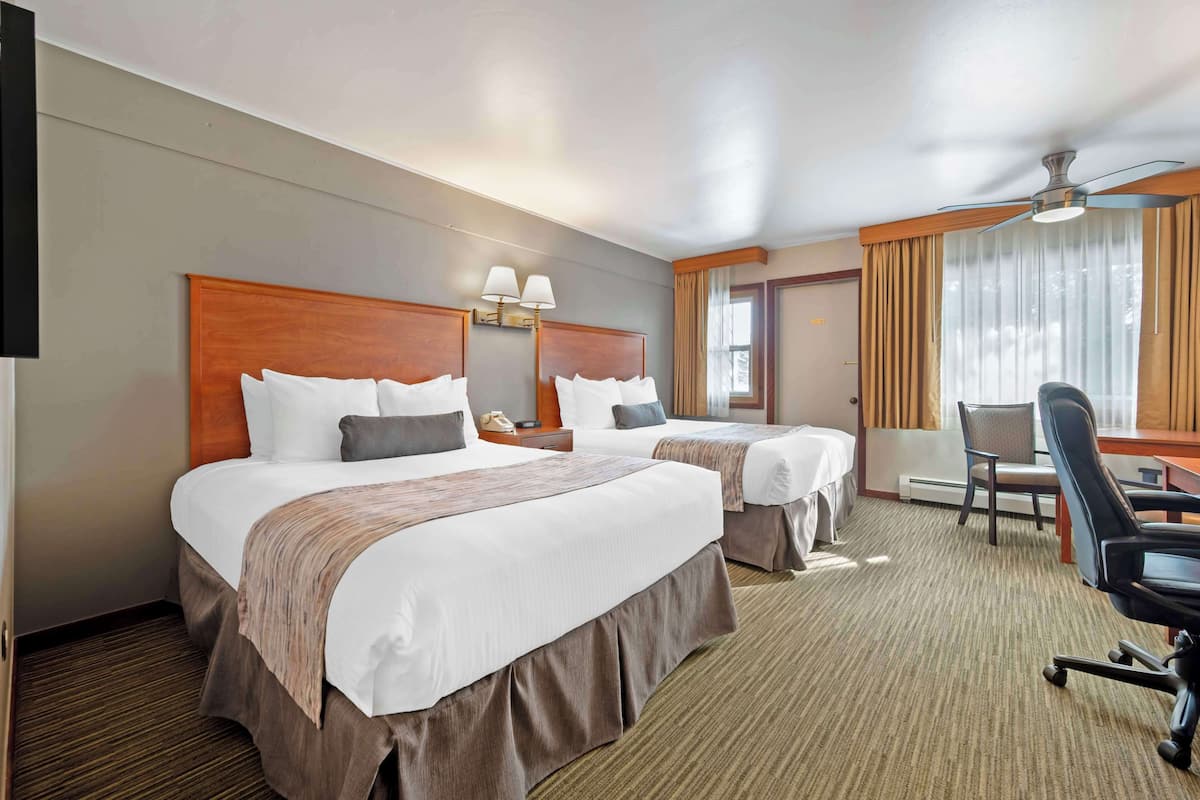 Ein Hotelzimmer mit zwei Betten, einem Schreibtisch, einem Sessel, einem Deckenventilator und einem Fenster mit Vorhängen.