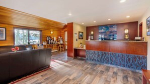 A reception area with a wooden reception desk, a seating area with a sofa, and a view of the outdoors through large windows. - Best Western Ptarmigan Lodge (Dillon)