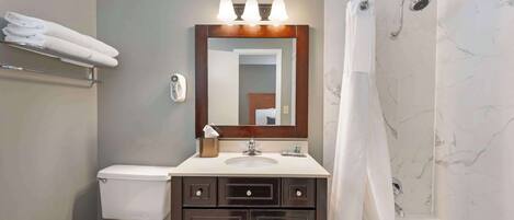 A bathroom with a toilet, sink, vanity with drawers, a mirror, a shower with a curtain, and a towel rack with folded towels.