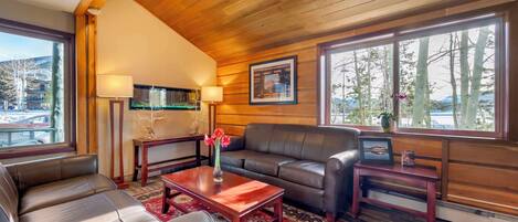 A cozy living room with a wooden ceiling, leather sofa, and a red patterned rug.