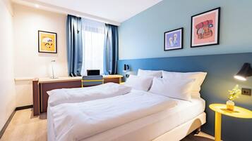 Habitación de hotel con una cama grande, un escritorio, una silla y una mesita de noche con una lámpara.