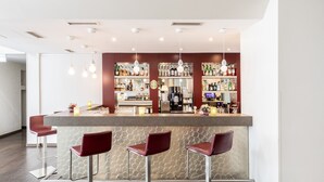 A modern bar area with a counter, bar stools, and a well-stocked shelf of beverages. - Garner Hotel Osnabruck by IHG (Osnabrueck)