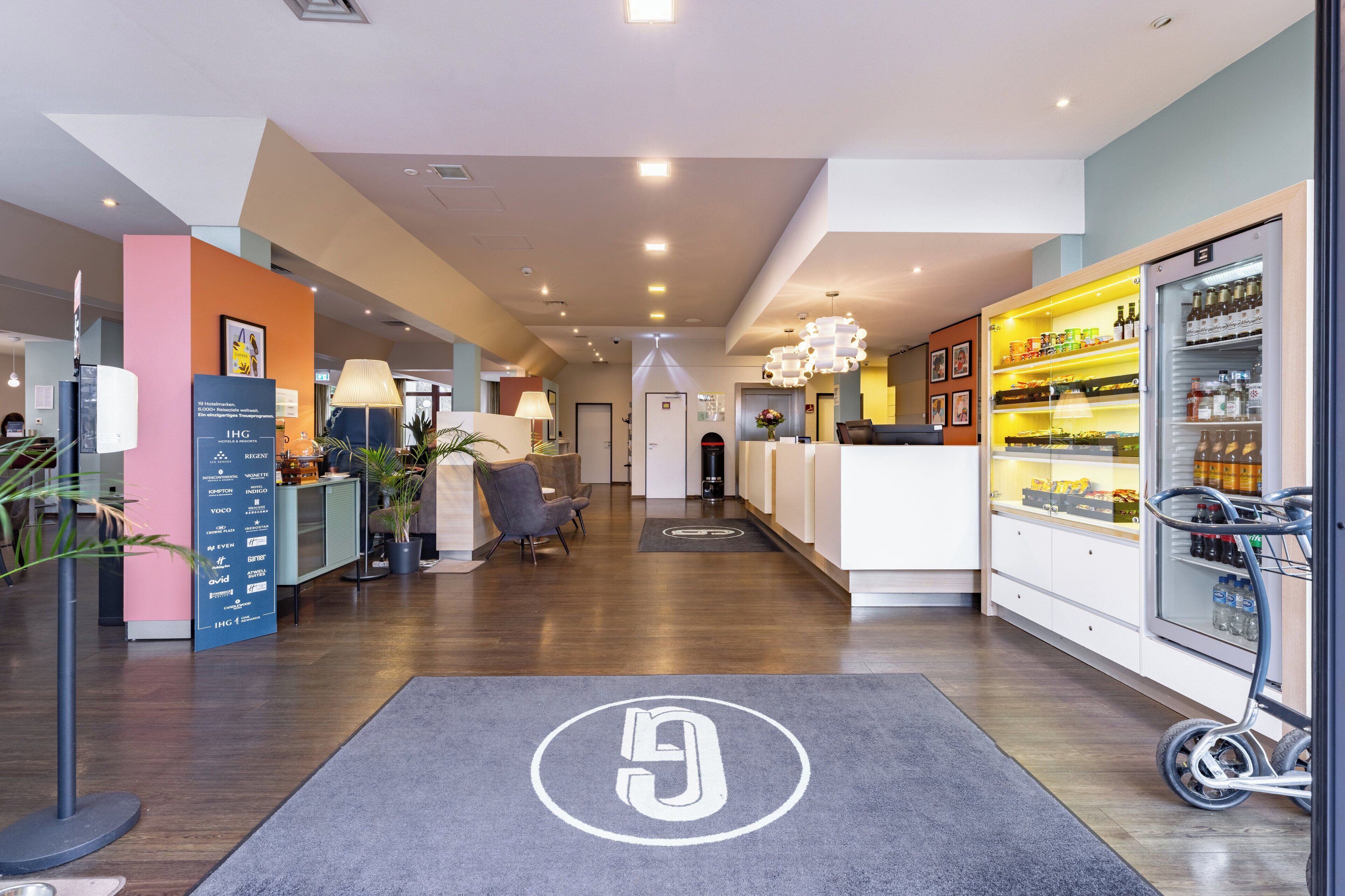 A hotel lobby with a reception desk, seating area, and a refrigerator stocked with beverages.