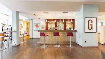 A modern bar area with a counter and three red bar stools. There is a framed letter 'G' on the wall to the right.