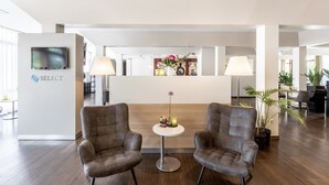 A modern hotel lobby with two plush armchairs, a reception desk, and a TV mounted on the wall. - Garner Hotel Osnabruck by IHG (Osnabrueck)
