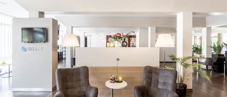 Un hall d’hôtel moderne avec deux fauteuils confortables, un comptoir d’accueil et un téléviseur fixé au mur.