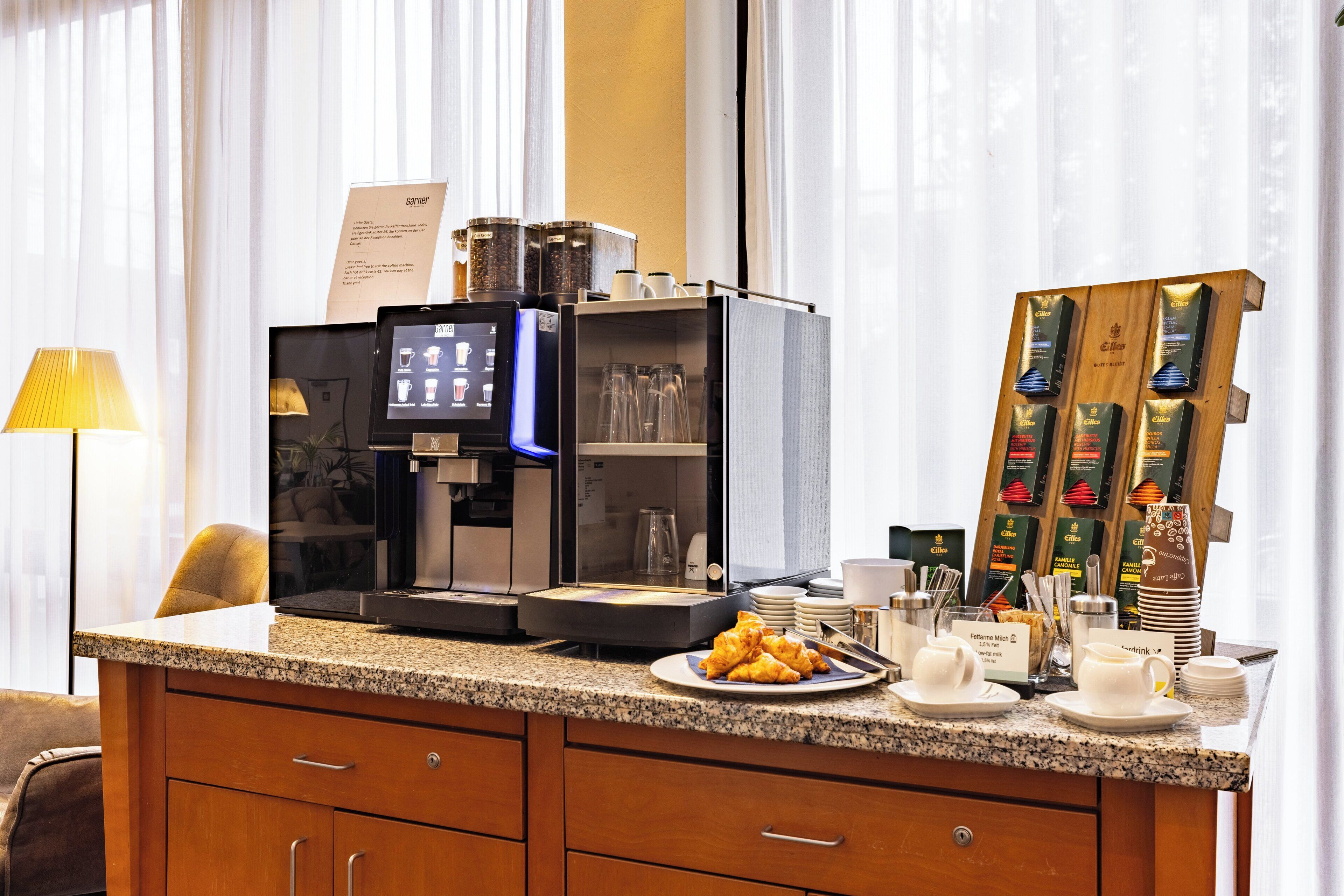 A hotel room with a coffee station featuring a coffee machine, a variety of coffee pods, and a plate of croissants.