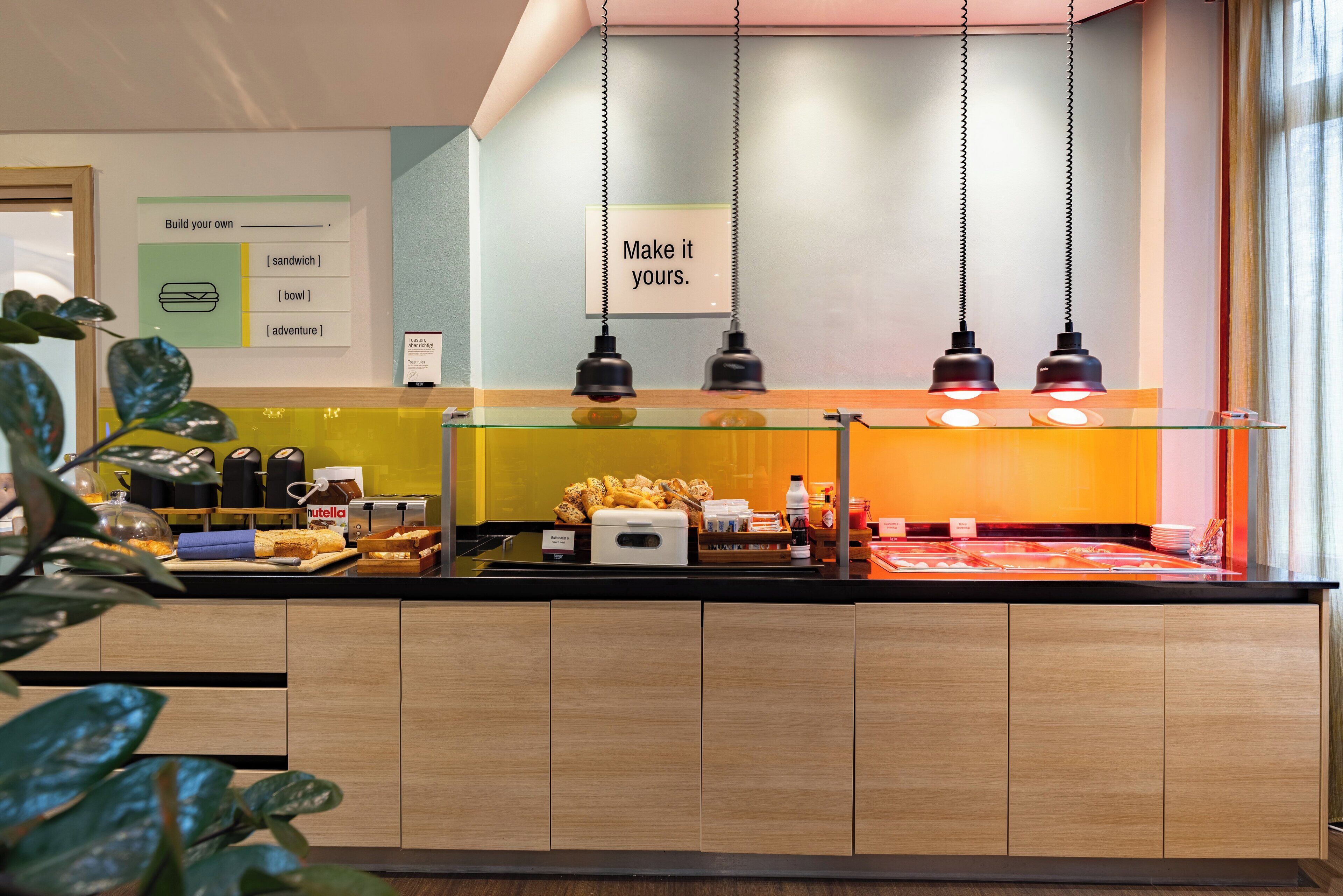 Un buffet pour le petit-déjeuner proposant une variété d’aliments, un panneau invitant les clients à personnaliser leur repas et un éclairage suspendu.