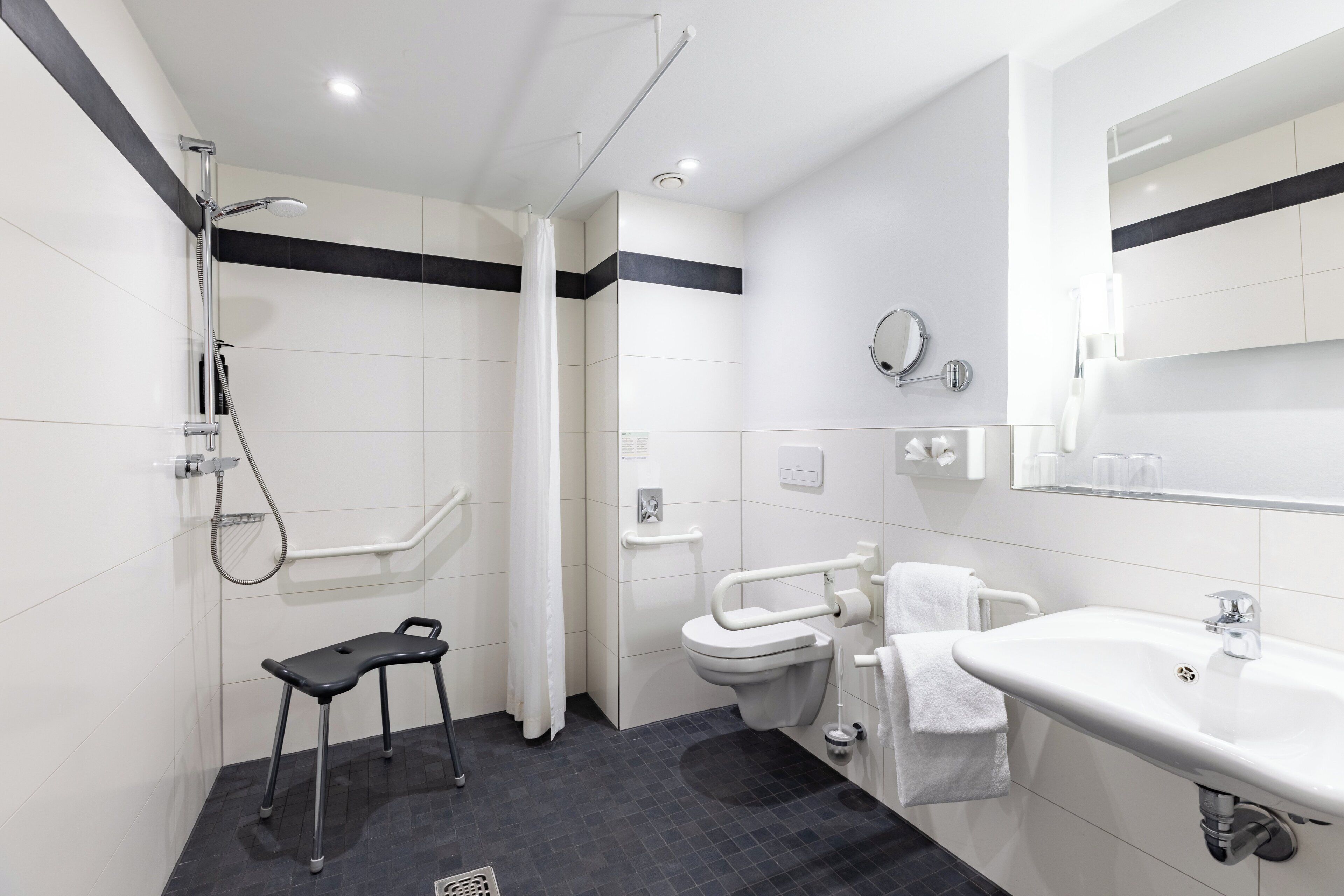 Un bagno moderno con doccia, WC e lavandino, caratterizzato da una palette di colori bianco e nero e dotata di una barra di sostegno per l'accessibilità.