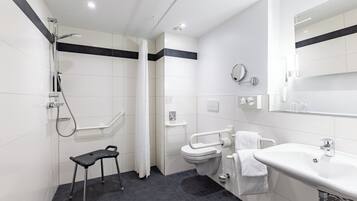 Un bagno moderno con doccia, WC e lavandino, caratterizzato da una palette di colori bianco e nero e dotata di una barra di sostegno per l'accessibilità.