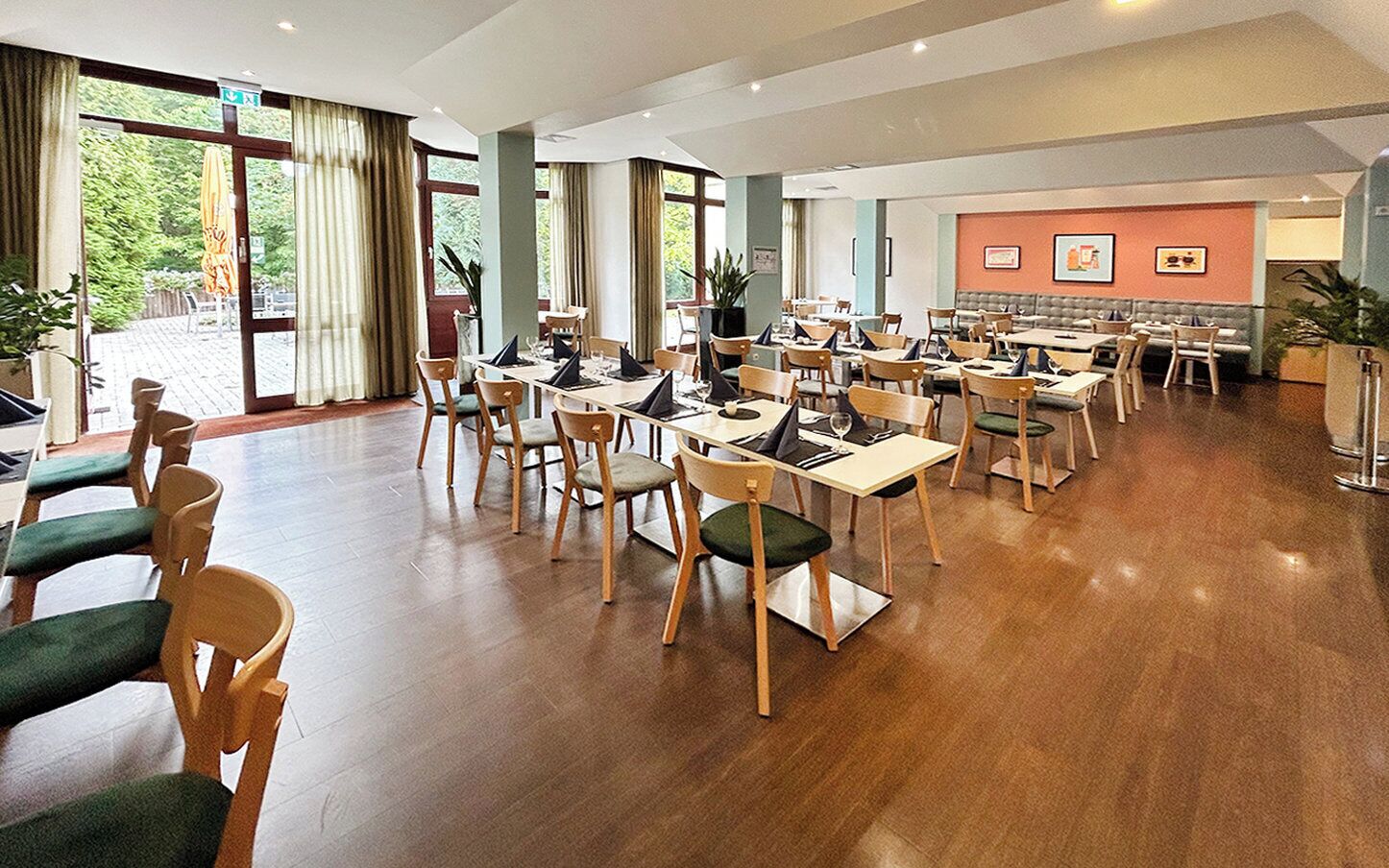 A spacious dining area with wooden tables and chairs, large windows with curtains, and a seating area with a sofa and chairs.