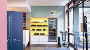 A store interior with shelves stocked with snacks and beverages, a refrigerated section, and a shopping cart. - Garner Hotel Osnabruck by IHG (Osnabrueck)