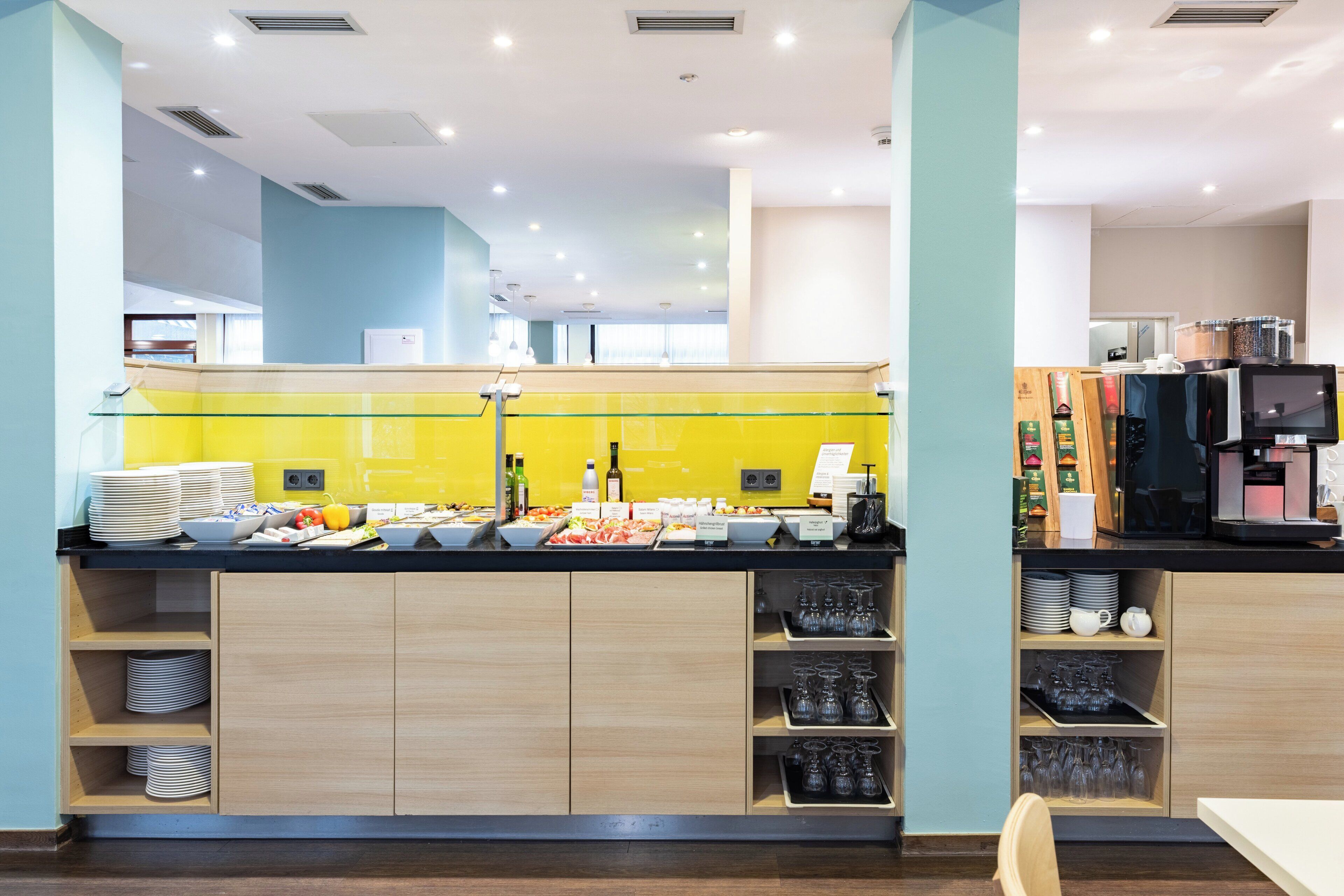 A modern breakfast bar with a yellow backsplash, wooden cabinets, and a variety of breakfast items.