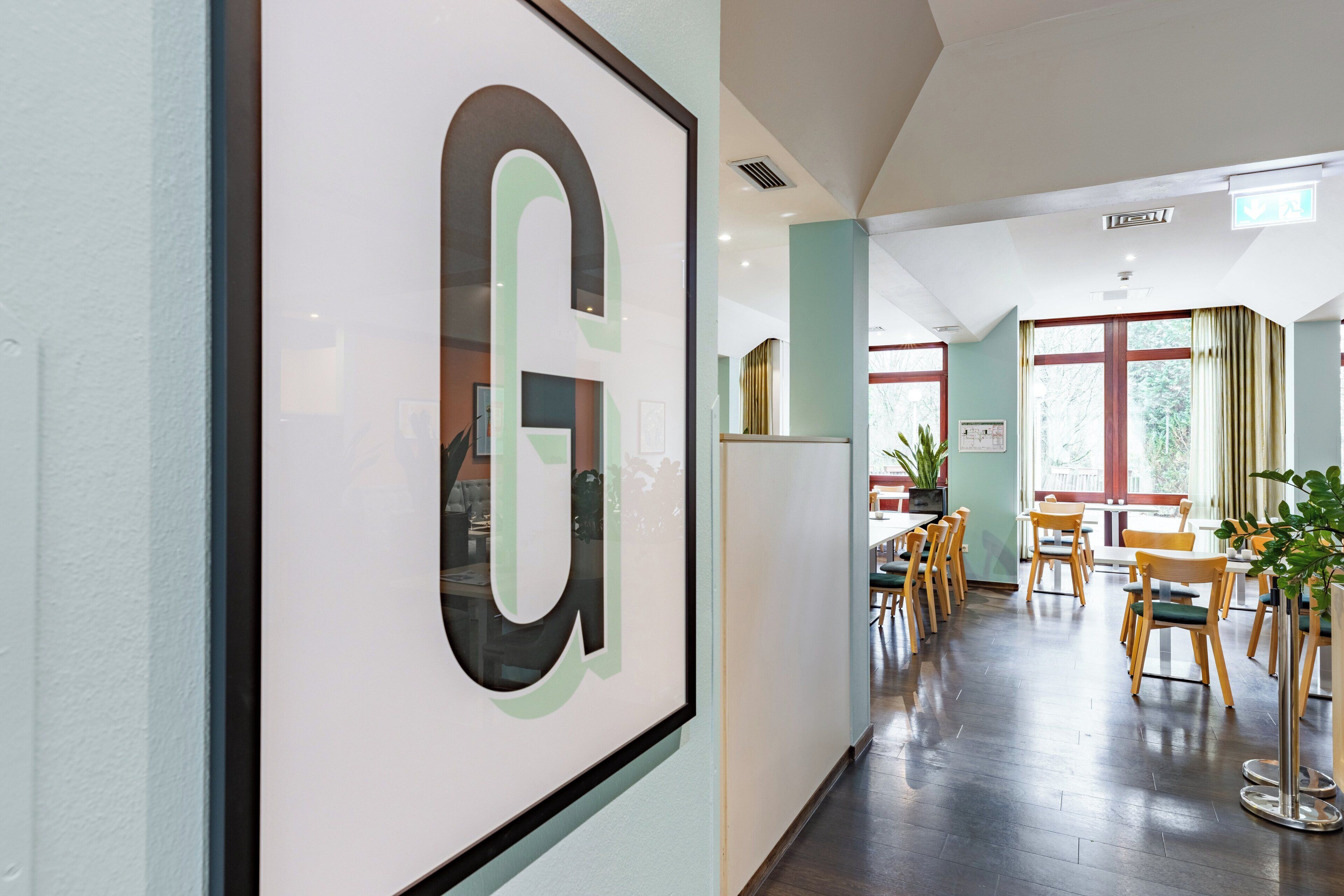 A hallway with a framed 'G' sign, wooden chairs, and tables in a dining area.