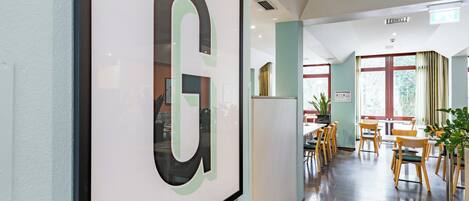 A hallway with a framed 'G' sign, wooden chairs, and tables in a dining area.