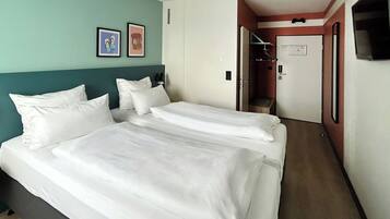 Habitación de hotel con dos camas, una pared verde azulado y una puerta que da a un baño.