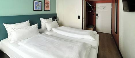 Habitación de hotel con dos camas, una pared verde azulado y una puerta que da a un baño.