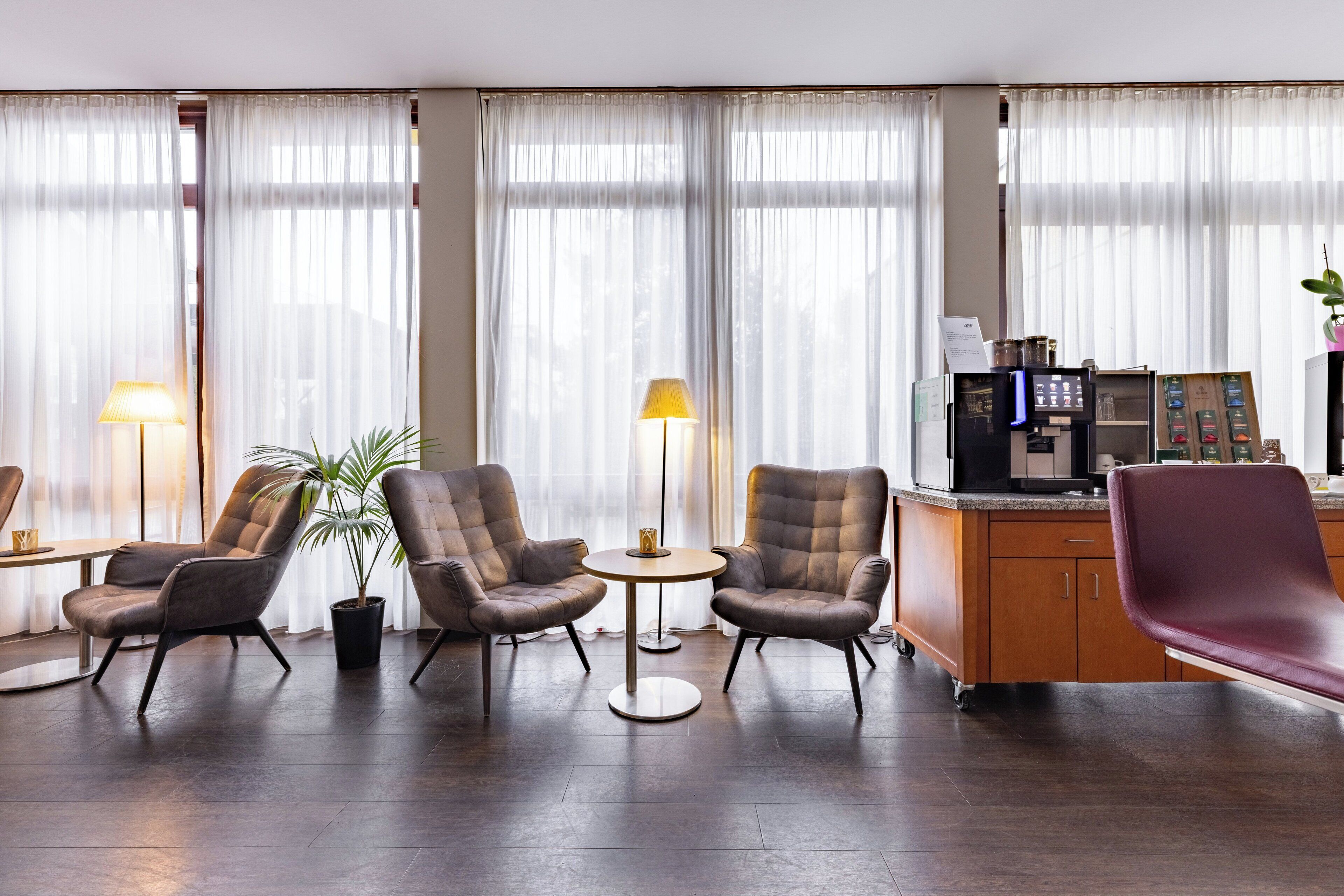 A hotel lobby with leather armchairs, a small round table, a coffee machine, and a potted plant.