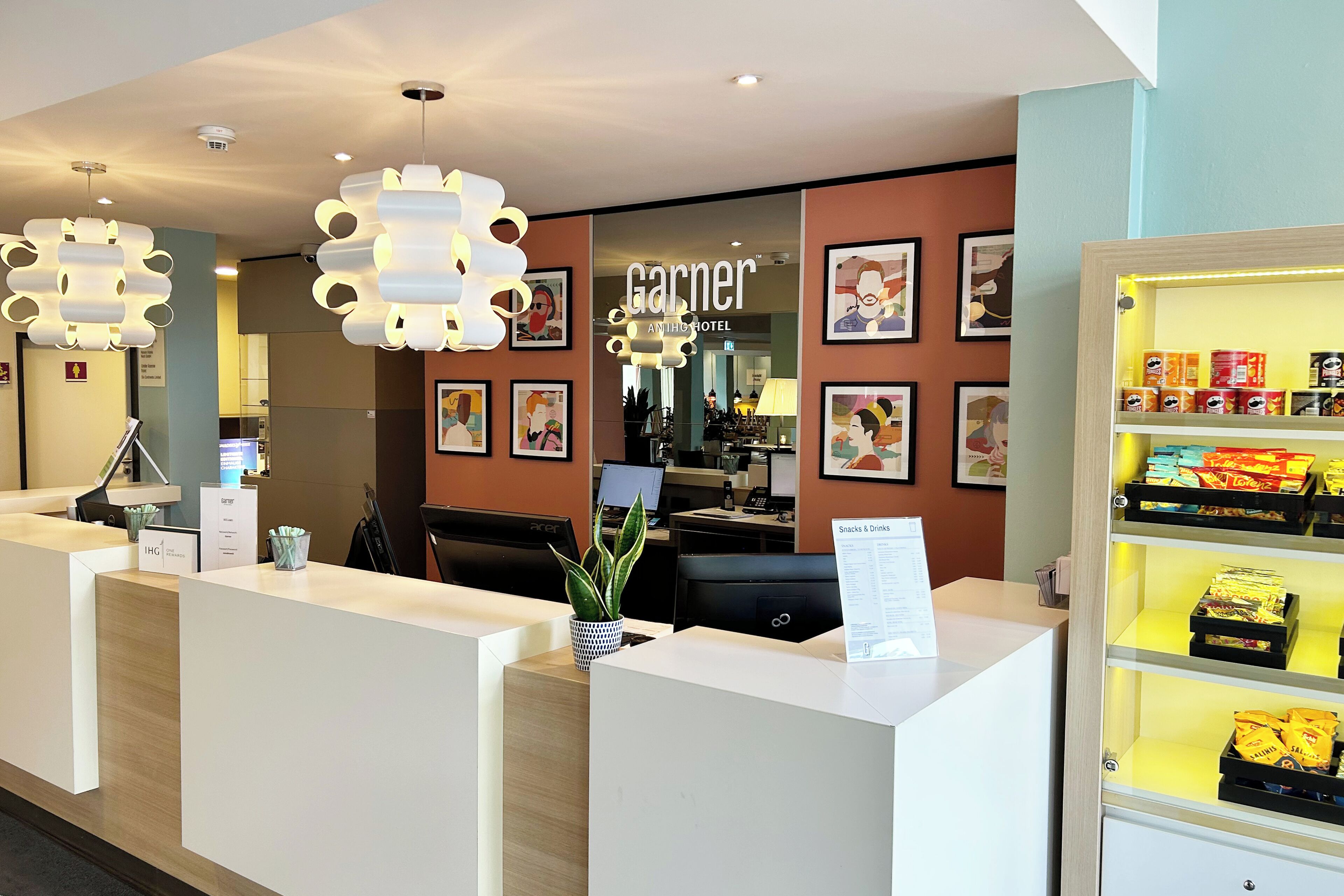 A hotel reception area with a modern design, featuring a reception desk, framed artwork on the walls, and a snack display.