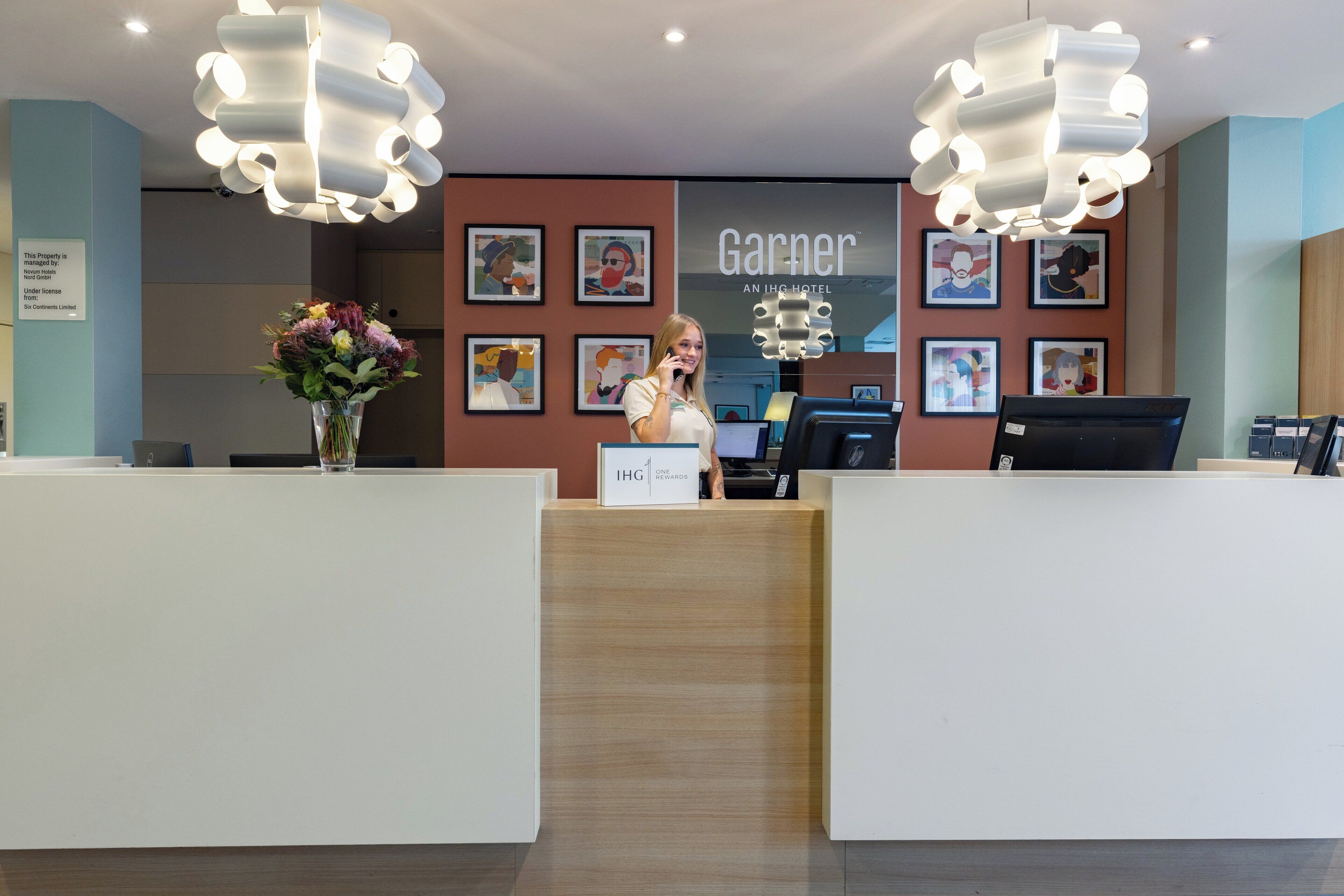 A hotel reception area with a modern design, featuring a wooden reception desk, a large chandelier, and framed artwork on the walls.