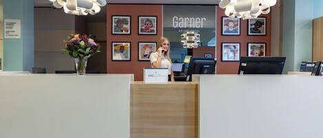 A hotel reception area with a modern design, featuring a wooden reception desk, a large chandelier, and framed artwork on the walls.