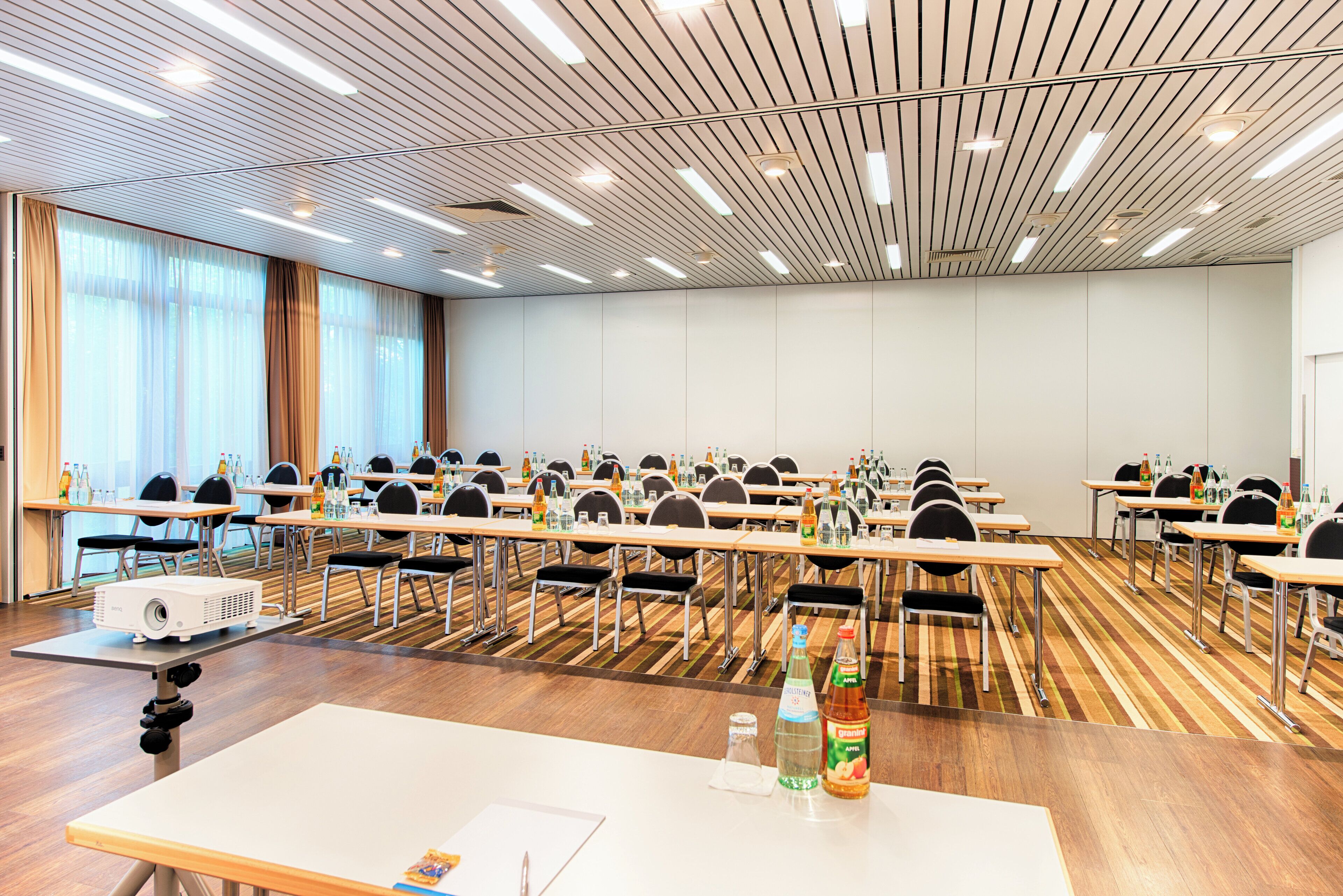 Une salle de conférence avec des rangées de tables et de chaises, équipée de projecteurs et de bouteilles d’eau.