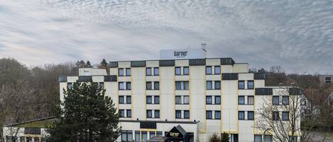 Un hotel de varios pisos con un llamativo letrero 'Garner', que presenta un diseño arquitectónico moderno con techo plano y fachada simétrica.