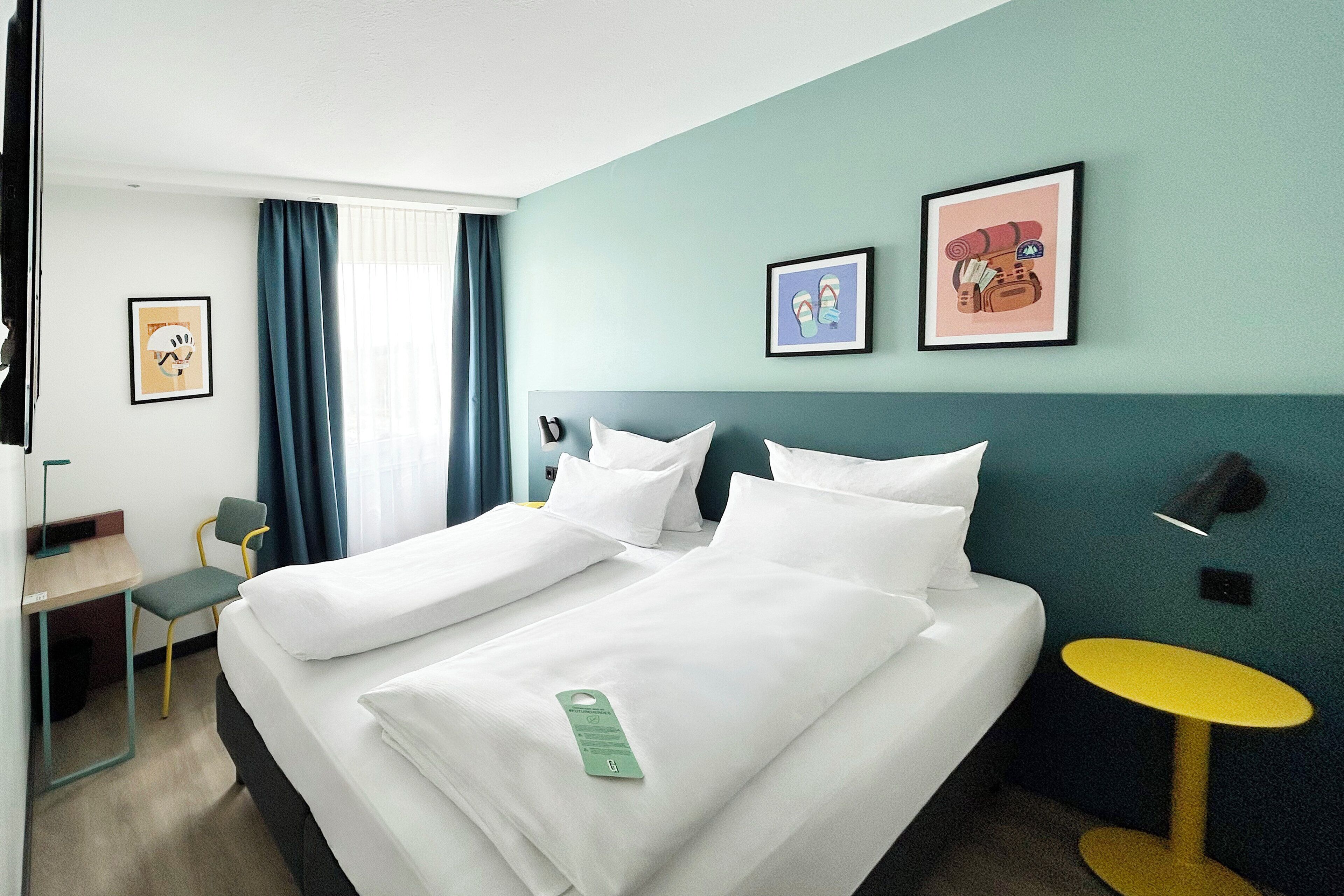 Habitación de hotel con cama, escritorio, silla, una mesita y obras de arte en las paredes.