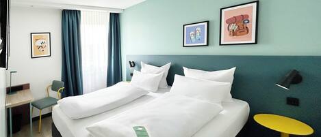 Habitación de hotel con cama, escritorio, silla, una mesita y obras de arte en las paredes.