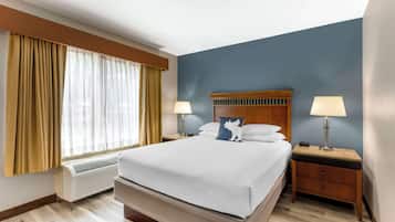 Una habitación de hotel con una cama grande, dos mesitas de noche con lámparas, una ventana con cortinas y un aire acondicionado integrado.