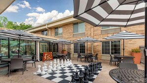 An outdoor patio with chess tables and umbrellas, brick walls, and large windows. - Best Western Denver Southwest (Lakewood)
