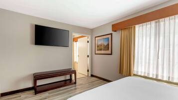 A hotel room with a bed, a bench, a flat-screen TV, a painting, and a window with curtains.