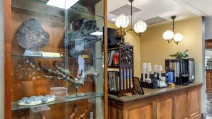 A reception area with a glass display case containing various fossils and artifacts, a wooden reception desk, a globe, and a coffee machine. - Best Western Denver Southwest (Lakewood)