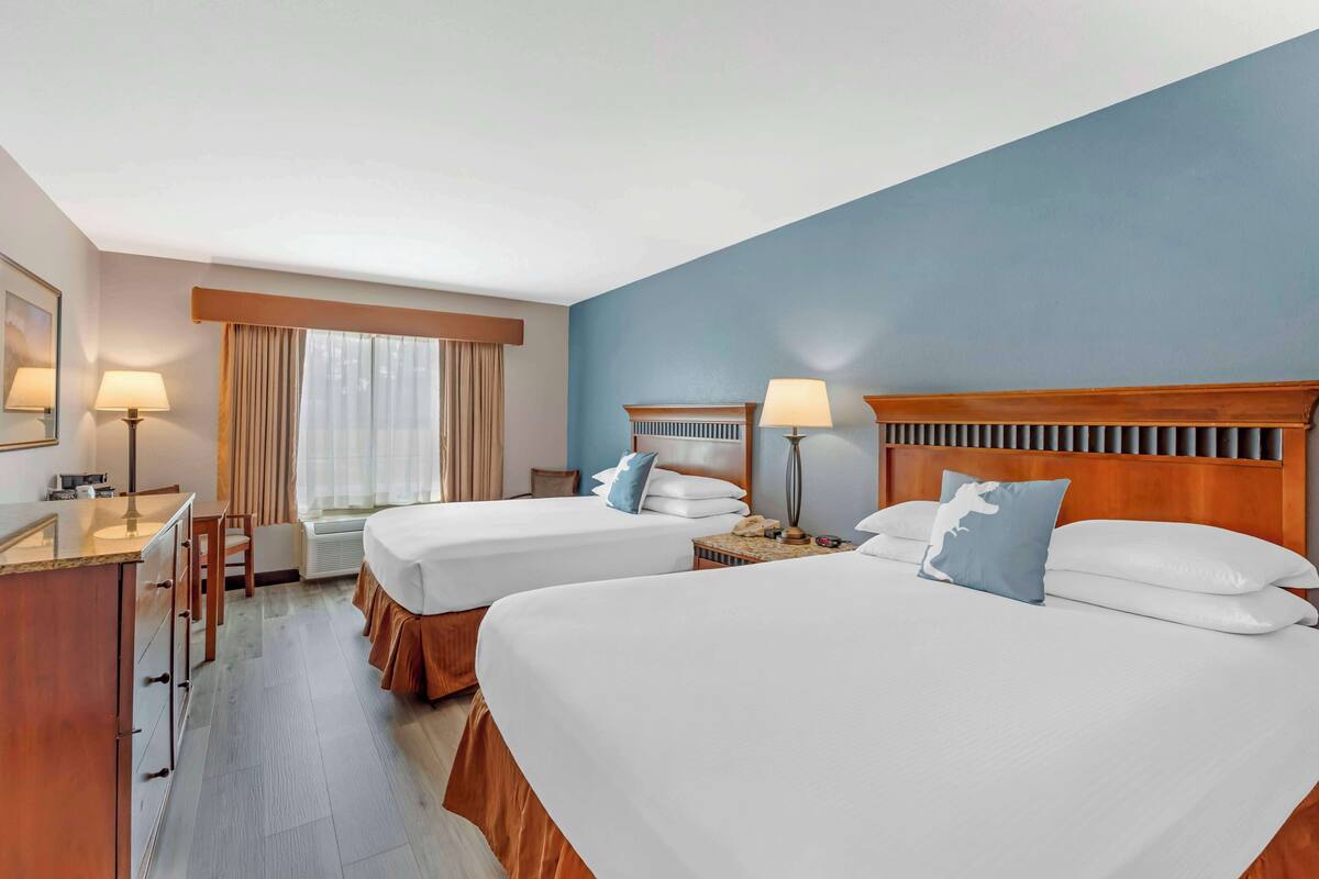 A hotel room with two beds, a desk, a chair, a vanity, and a window with curtains.