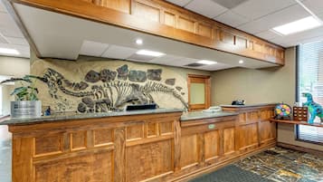 Ein Empfangsbereich mit einem Holzbüro, einer Steinwand mit Fossilienabdrücken, einer Pflanze und einer Dinosaurierfigur.