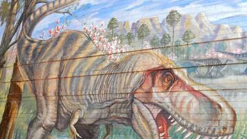Een muurschildering van een dinosaurus met een rivier en bergen op de achtergrond.
