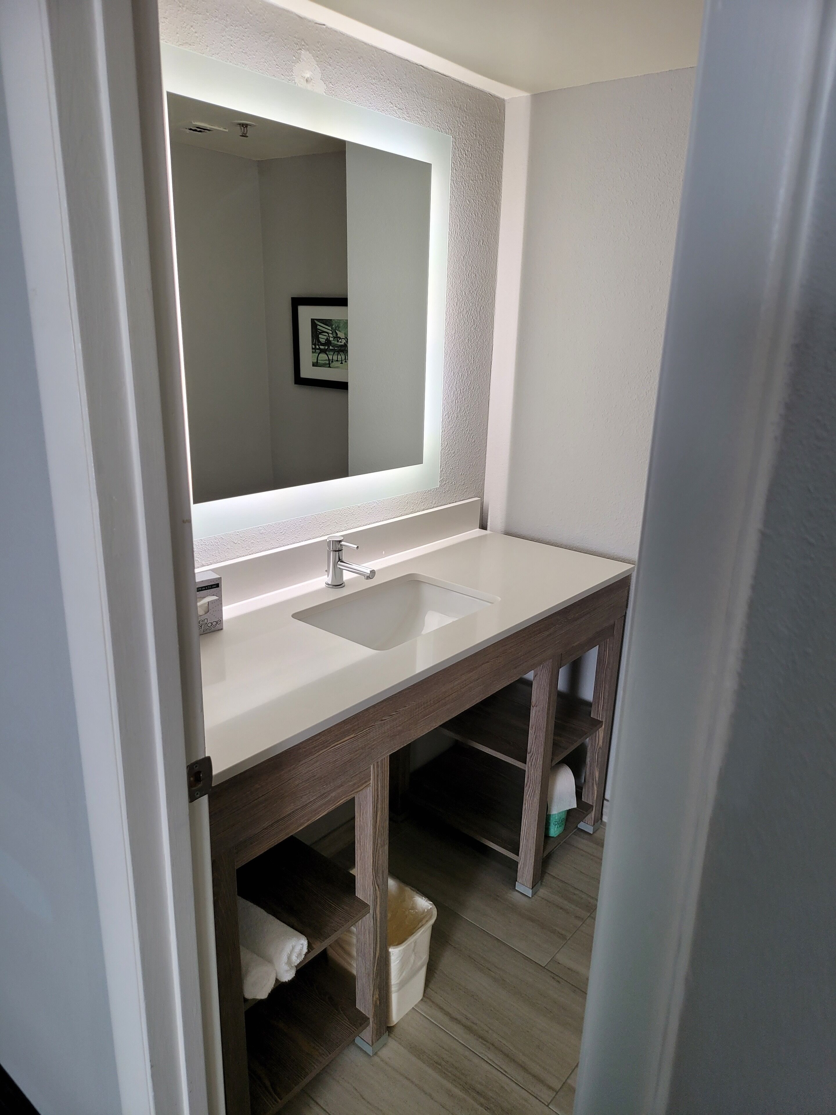 A bathroom with a white sink, a large mirror, and a wooden vanity.