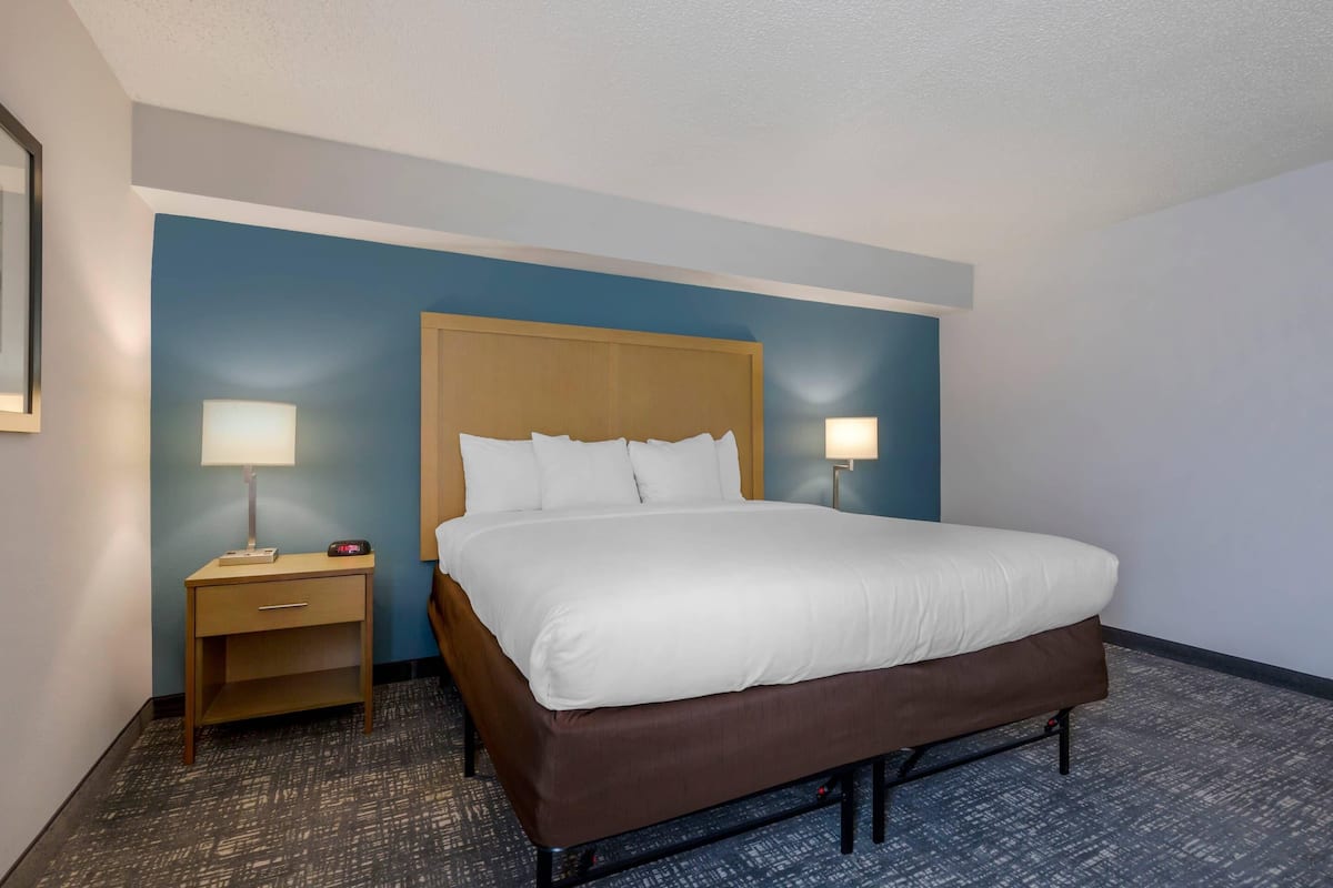 A hotel room with a large bed, two bedside lamps, a wooden nightstand, and a carpeted floor.