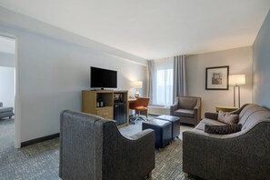 A hotel room with a flat-screen TV, a desk with a chair, two armchairs, a sofa, and a lamp.